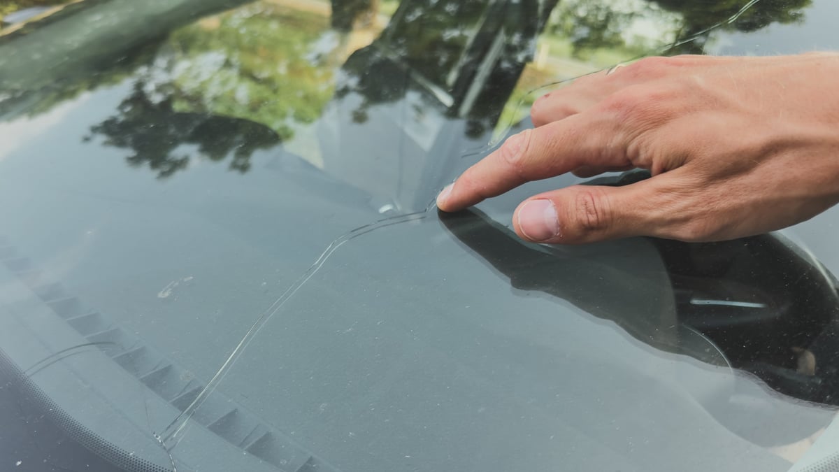 Close-up of a hand pointing at a long crack in a car windscreen